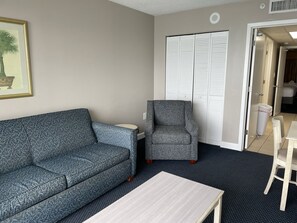 A room with a patterned sofa, a chair, a small table, and a closet with louvered doors. - Oceanfrnt 2Q 1BR Suite. Resort w/Lazy River, Pools (Myrtle Beach)