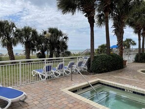 A poolside area with lounge chairs, a pool, and a view of the beach.