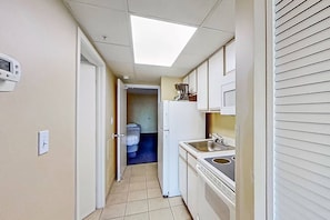A narrow hallway leading to a kitchen with a skylight, a refrigerator, and a sink.