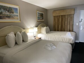 Ein Hotelzimmer mit zwei Betten, einem Nachttisch mit Lampe, einem Bild mit Strandmotiv und einer Tür mit Schloss.