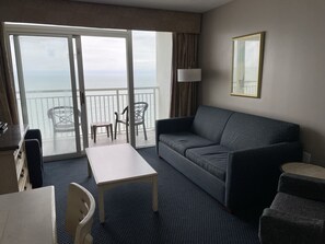 A hotel room with a balcony, a sofa, a table, and a chair.
