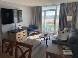 A hotel room with a flat-screen TV, a desk with a laptop, two chairs, a sofa, a small table, and a balcony with a view of the beach. - OCEANFRONT 3BR 2BA 1K1 Lazy River and Pools Resort (Myrtle Beach)