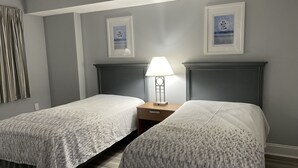 Une chambre d’hôtel avec deux lits, une table de chevet avec une lampe et deux tableaux encadrés au mur.
