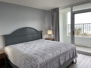 A bedroom with a bed, a nightstand, a lamp, and a view of the sea through a sliding glass door. - Oceanfront 3BR/2BA - Lazy River and Pools Resort (Myrtle Beach)