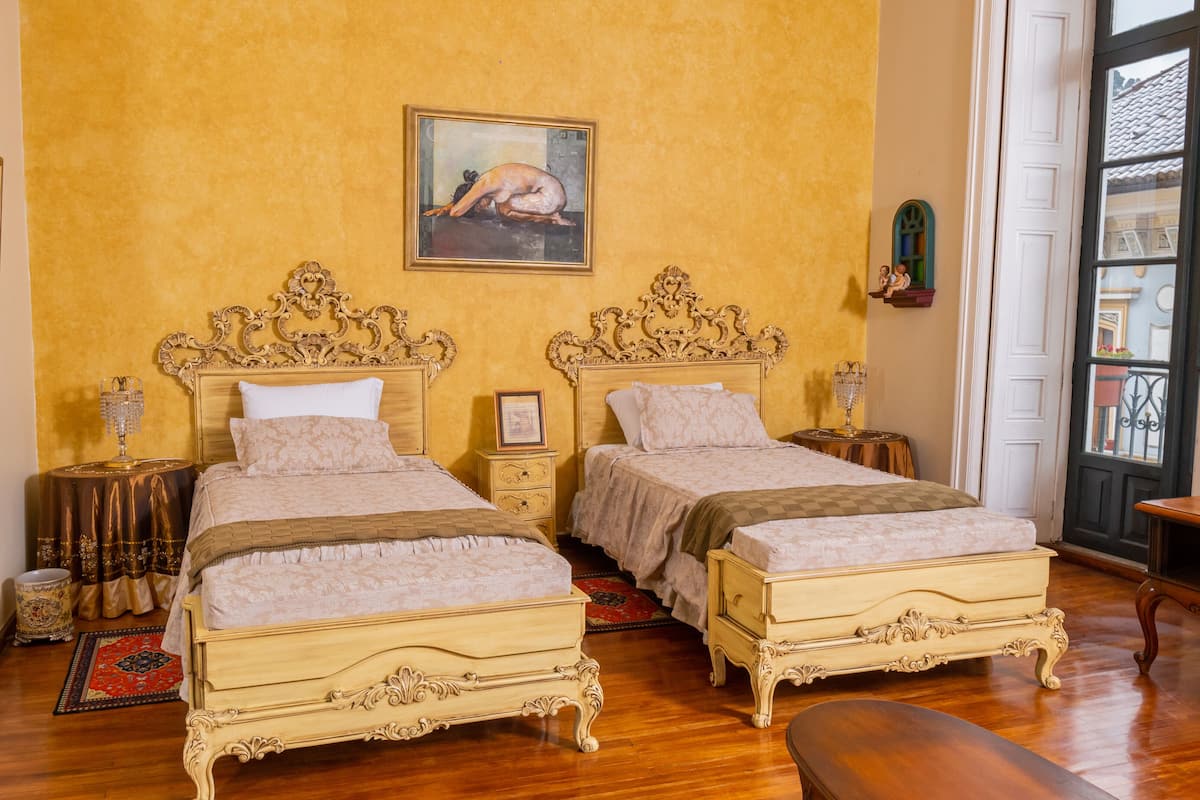 Une chambre d’hôtel avec deux lits richement décorés, un tableau au mur et une vue par la fenêtre.