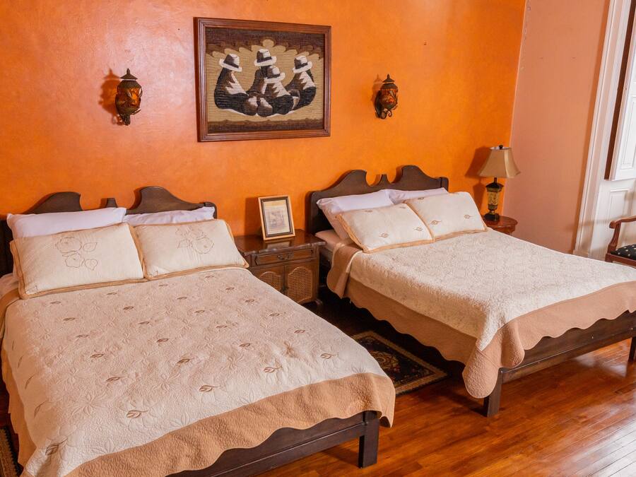 A hotel room with two beds, wooden headboards, a framed artwork on the wall, and a window with a view.