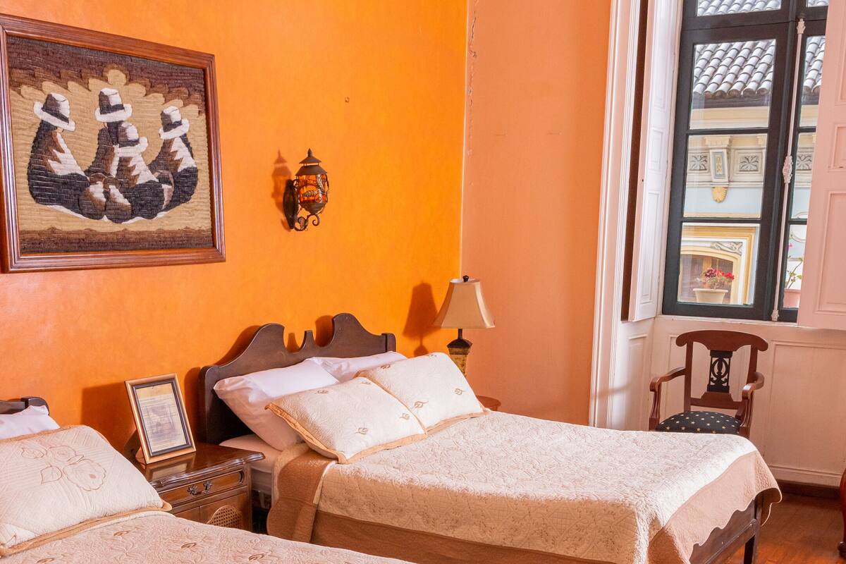 Une chambre avec deux lits, un plancher en bois, un tableau au mur et une fenêtre donnant sur des immeubles.