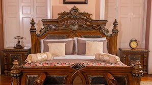A classic bedroom with a large ornate bed, a framed floral artwork above the bed, and a vintage telephone on the nightstand. - Casa Colonial Quito (Quito)