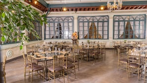 A spacious dining area with round tables and chairs, large windows with curtains, and a chandelier. - Casa Colonial Quito (Quito)