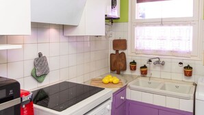 A kitchen with white cabinets, a black induction cooktop, a sink, and a window with lace curtains. - Nice apartment for 4 people with WIFI, TV and terrace (Calonge)
