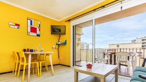 A bright yellow room with a wooden table and chairs, a TV mounted on the wall, and a balcony with a view of buildings. - Nice apartment for 4 people with WIFI, TV and terrace (Calonge)