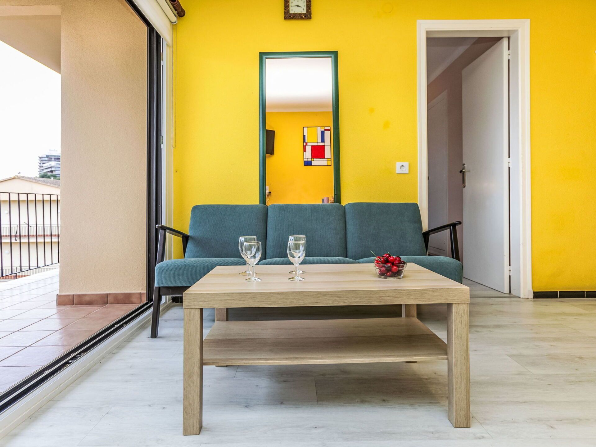 A balcony with a wooden table, two glasses, and a bowl of cherries.