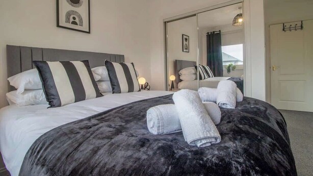 A hotel room with a bed, pillows, a dark blanket, and towels.