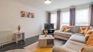 A modern living room with a sofa set, a coffee table, a TV, and artwork on the wall.