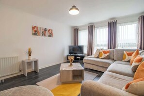 A modern living room with a sofa set, a coffee table, a TV, and artwork on the wall.