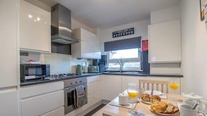 A modern kitchen with white cabinets, a stove, oven, and a dining table set with breakfast items.