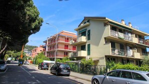 Un immeuble résidentiel à plusieurs étages doté de balcons, une rue bordée de voitures garées et des arbres qui bordent la route.