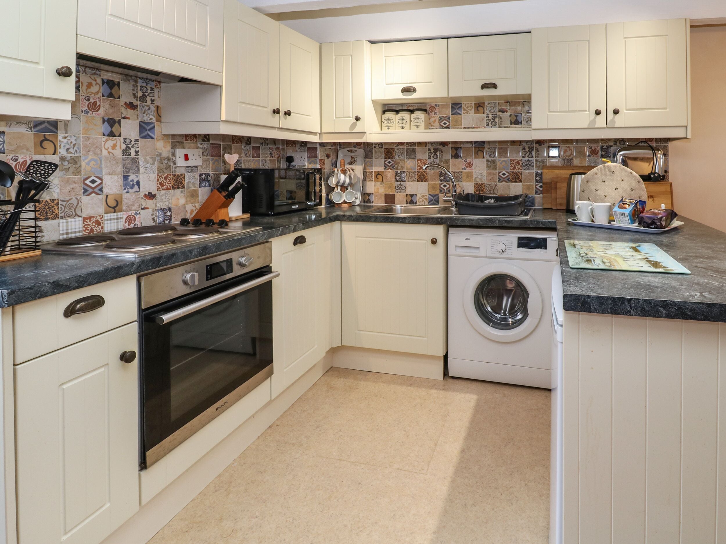 A kitchen with white cabinets, a microwave, a stove, a washing machine, and a tiled backsplash.
