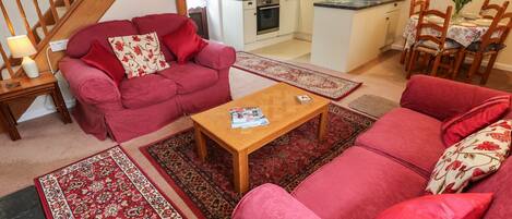 A living room with a red sofa, a wooden coffee table, and a kitchen in the background.