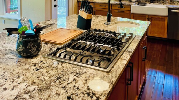 A kitchen with granite countertops, a gas stove, wooden cabinets, and pendant lighting.