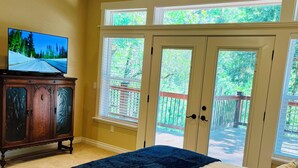 A bedroom with a large bed, a TV on a wooden cabinet, and a balcony with glass doors.