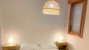 Un dormitorio con una cama, dos mesitas de noche con lámparas, un candelabro colgante, una ventana con persianas y baldosas de suelo estampadas.