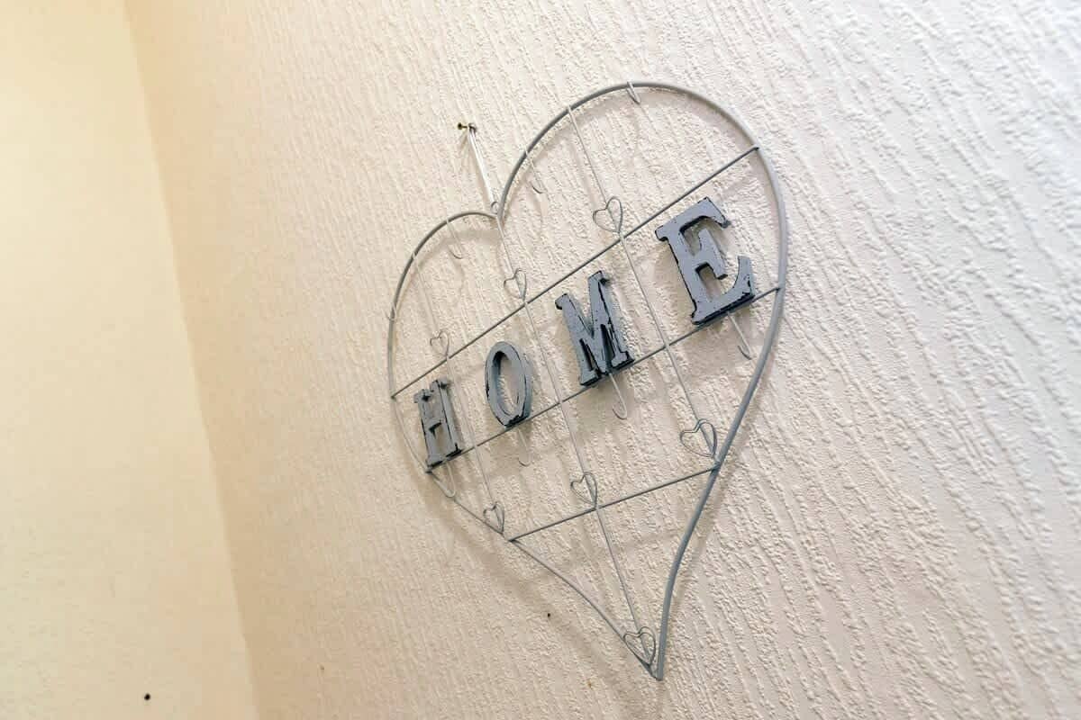 Et hjerteformet metalskilt med ordet 'HOME' på en væg med struktur.