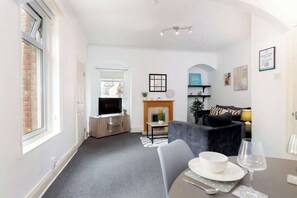 A modern living room with a fireplace, a television, and a dining area with a table set for two. - Spacious 2 Bedroom Home Near Newcastle City Centre (Gateshead)