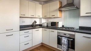 Una cocina moderna con gabinetes blancos, encimera negra, estufa a gas, microondas y horno empotrado.