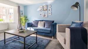 Una sala de estar con un sofá azul, un sofá beige, una mesa de centro y una lámpara de pie.