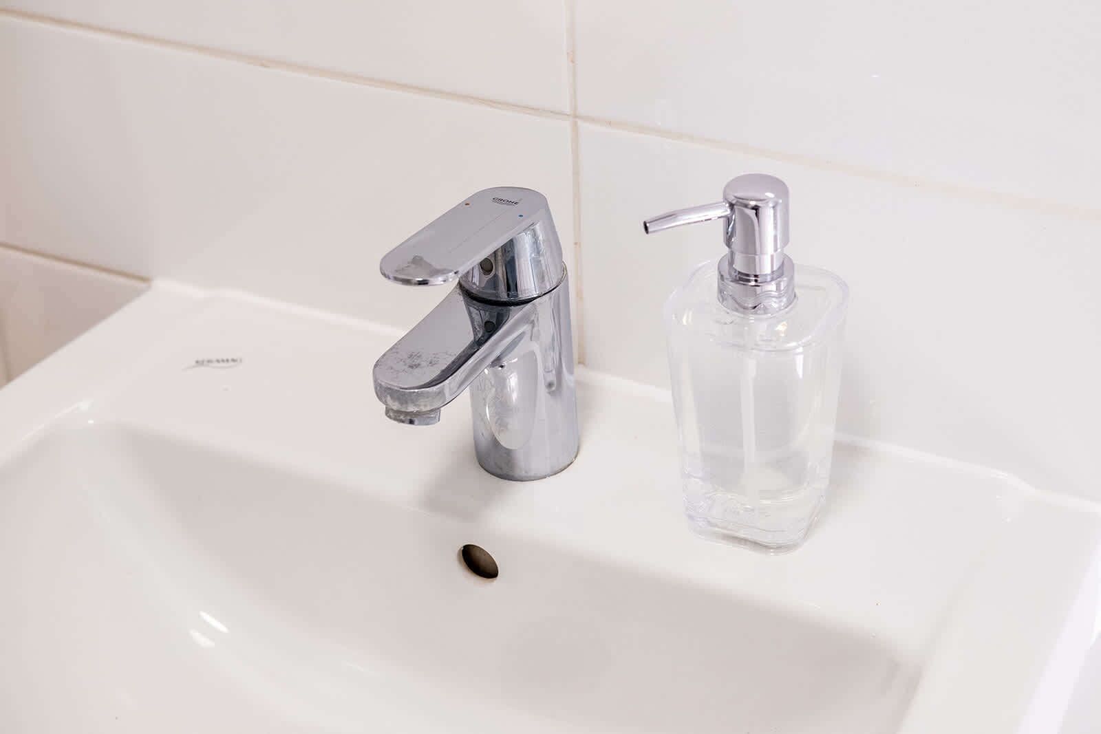 A bathroom sink with a chrome faucet and a clear soap dispenser.