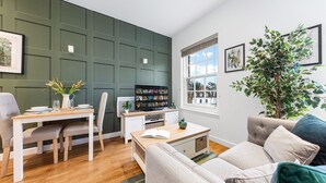 A modern living room with a dining area, a television, and a large window with a view of buildings. - Stunning 1 Bed Apartment Near Heathrow London (Staines)