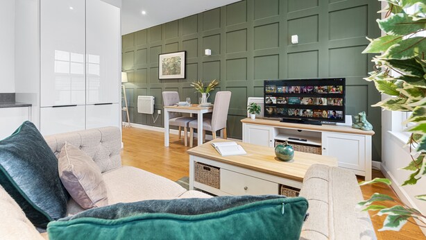 A modern living room with a sofa, a coffee table, and a TV displaying a video call. - Stunning 1 Bed Apartment Near Heathrow London (Staines)