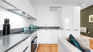 A modern kitchen with white cabinets, a black countertop, and a grey sofa with a green pillow. - Stunning 1 Bed Apartment Near Heathrow London (Staines)