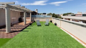 Eine Dachterrasse mit Kunstgrasanlage, zwei Liegestühlen und einer Pergola.