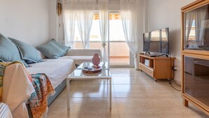 Ein modernes Wohnzimmer mit einer Couch, einem Couchtisch, einem Fernseher und einem Balkon mit Vorhängen.