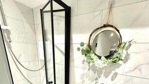 A modern bathroom with a glass shower enclosure, a white sink with a black faucet, and a mirror with a green plant decoration. - New Cross Suites -se14 (London)