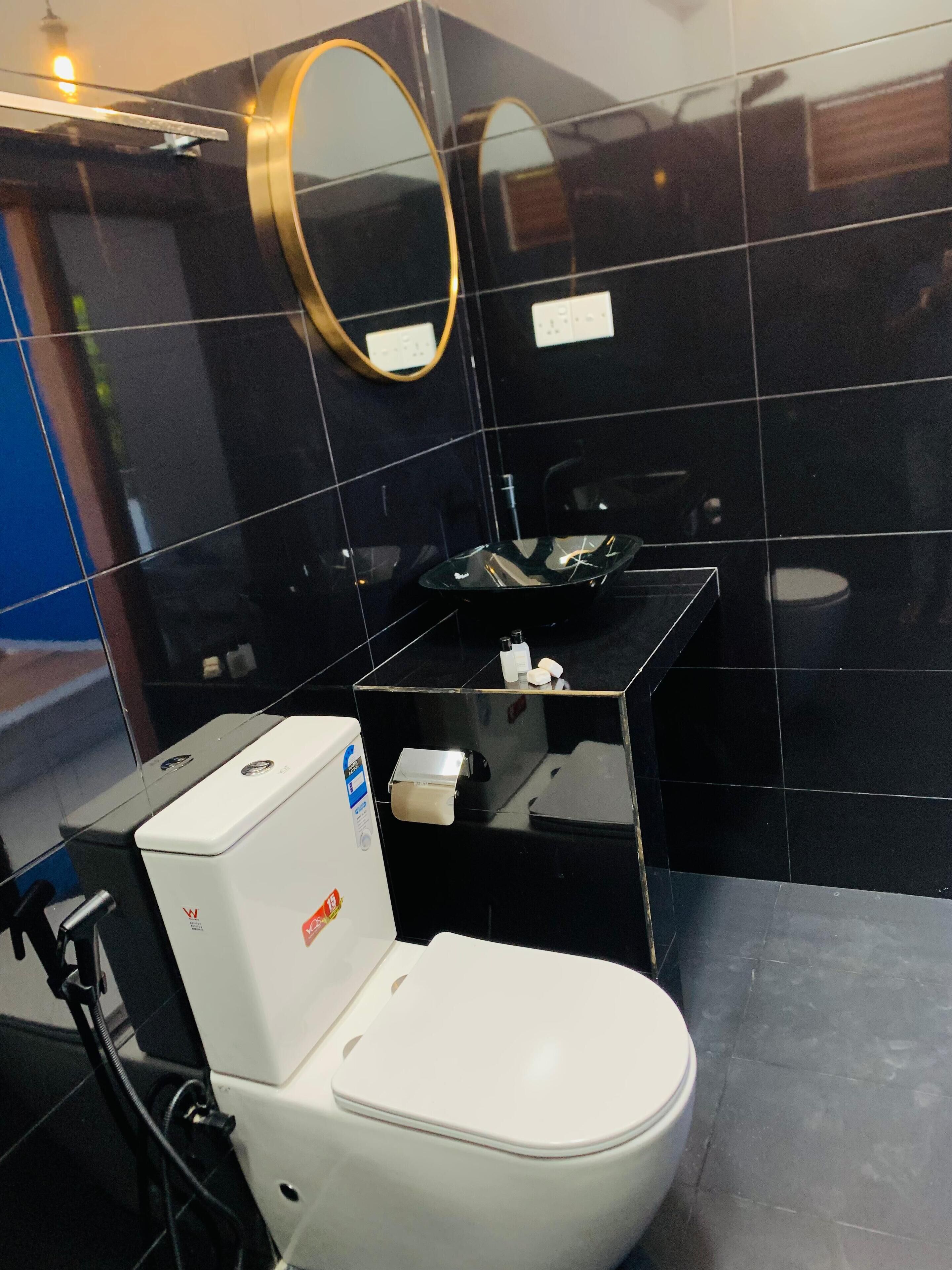 A modern bathroom with a white toilet, a black sink, and a mirror with a gold frame.