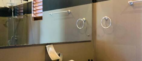 A modern bathroom with a large mirror, a white sink, and a wooden vanity.