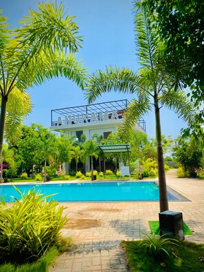 A hotel with a pool, surrounded by lush greenery and a clear blue sky. - Anukama Resort  (Nilaveli)