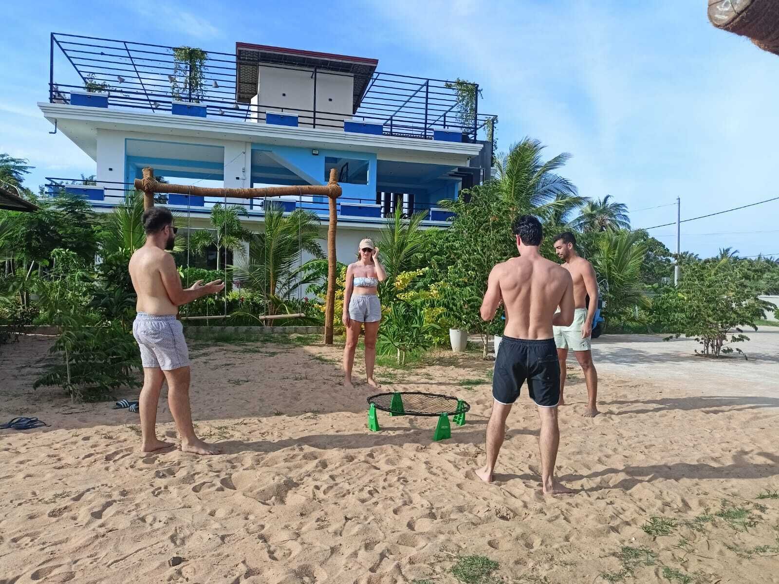 A beach with a building in the background, palm trees, and a volleyball net.