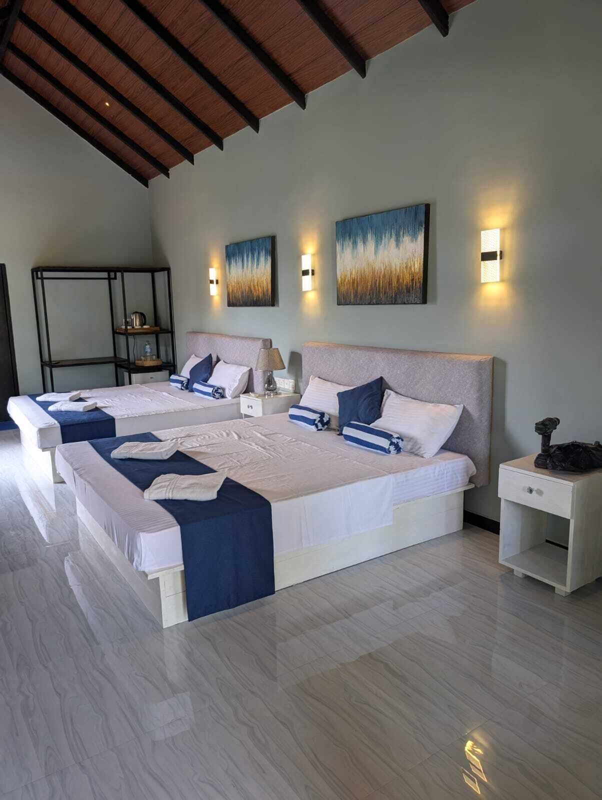 A hotel room with two beds, a nightstand, a lamp, and artwork on the walls.
