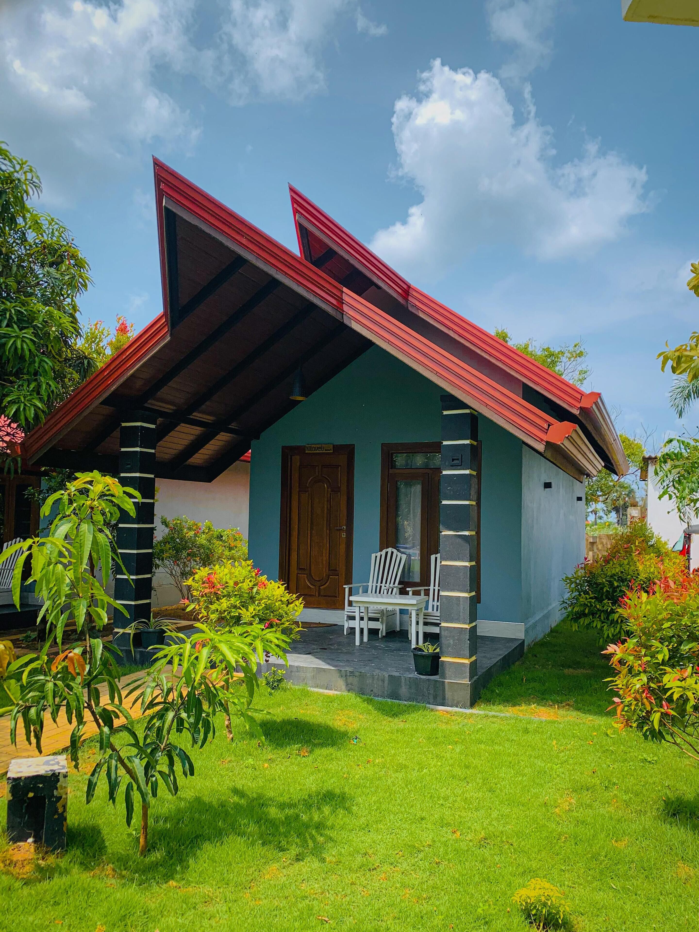 A two-story house with a red roof, a porch with white chairs, and a well-maintained garden.