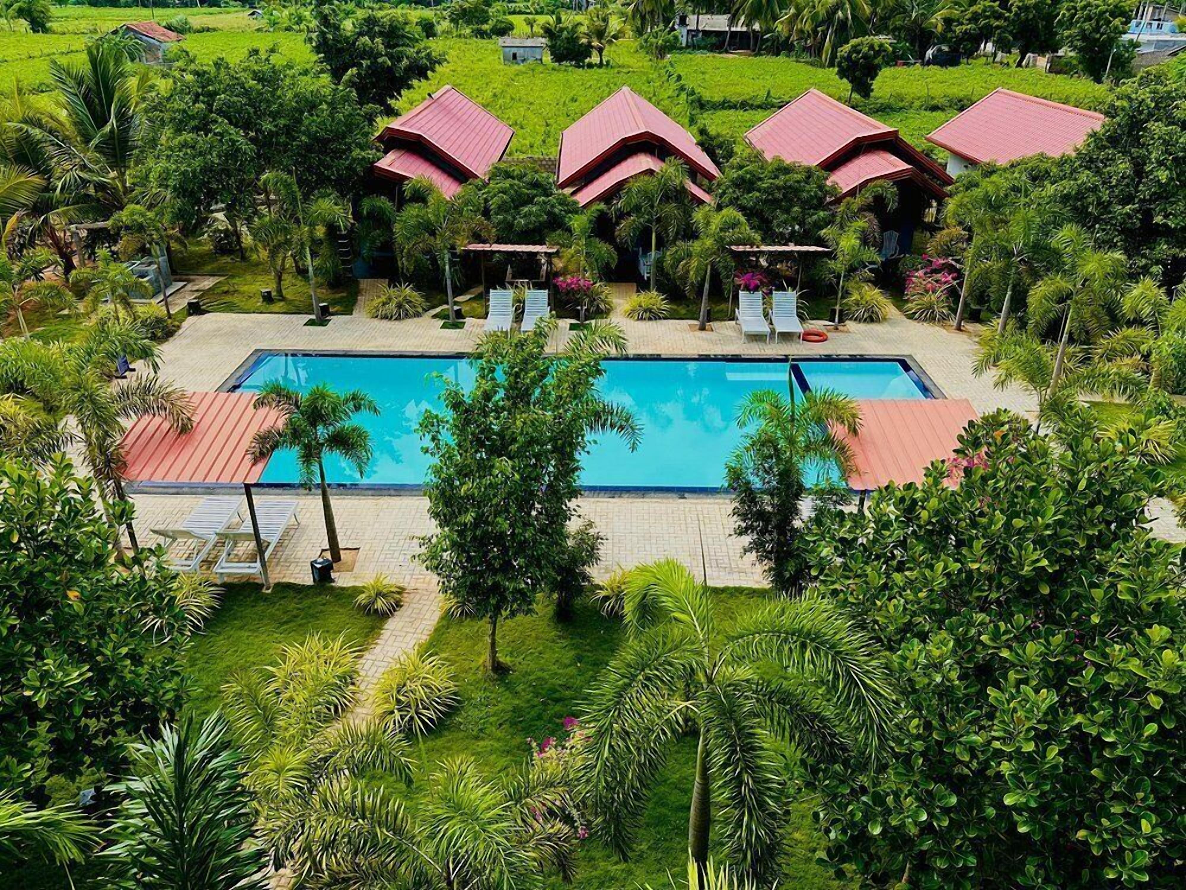 Ein Pool, umgeben von üppiger Vegetation und Gebäuden mit roten Dächern, wahrscheinlich Teil eines Resorts.