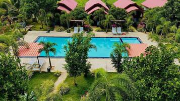 Ein Pool, umgeben von üppiger Vegetation und Gebäuden mit roten Dächern, wahrscheinlich Teil eines Resorts.