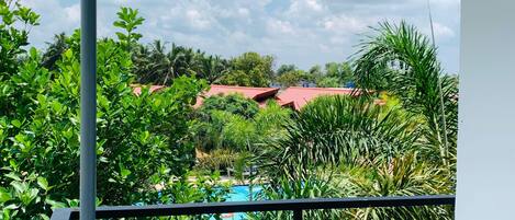 Un balcón con vista a una piscina, rodeado de exuberante vegetación y edificios con tejados rojos.