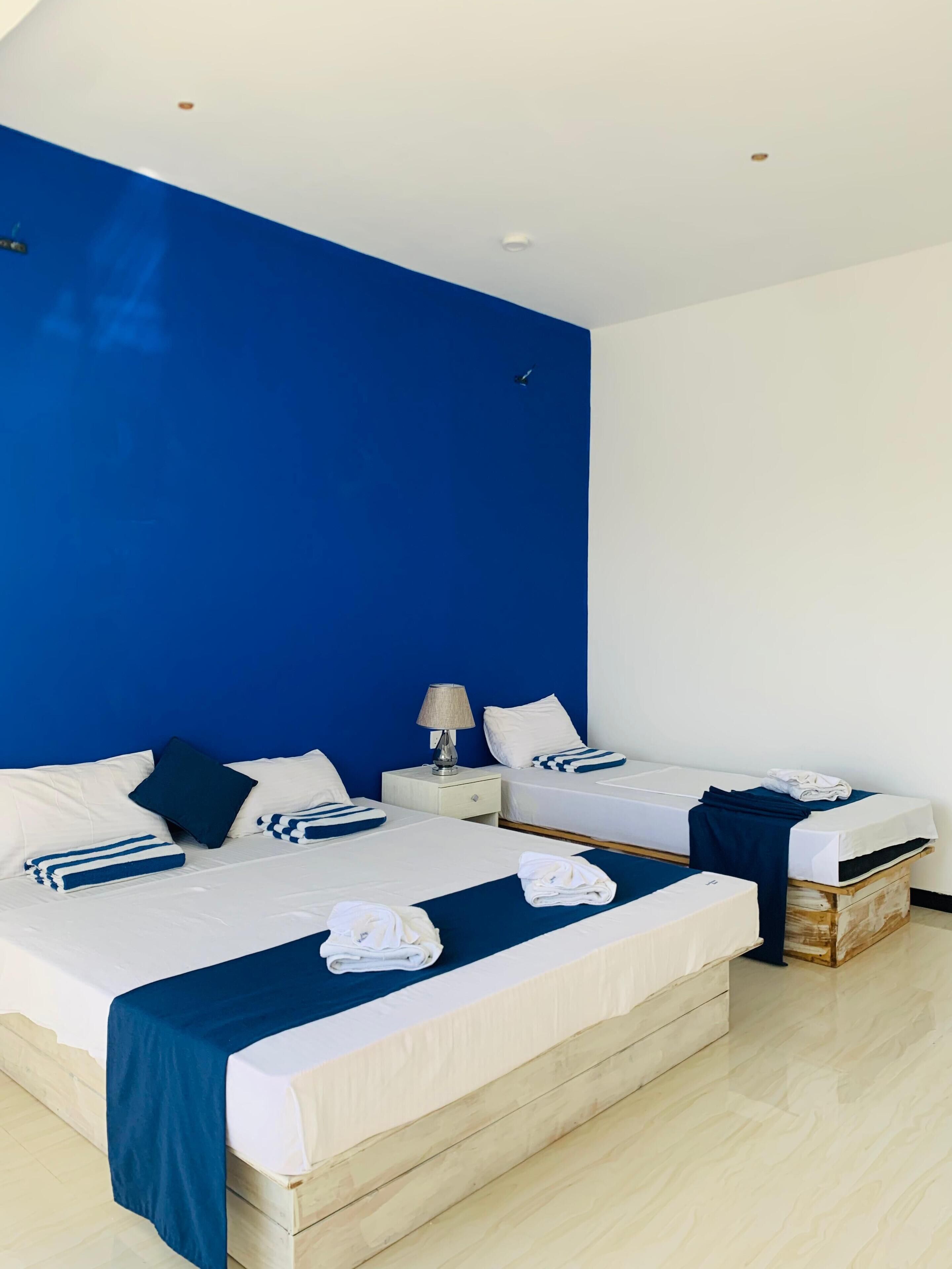 Quarto de hotel com duas camas, uma parede de destaque azul, roupa de cama branca e um penteado de madeira.