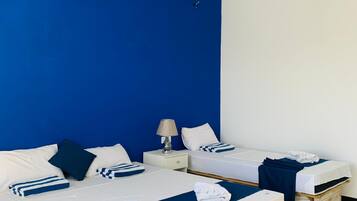Une chambre d’hôtel avec deux lits, un mur d’accent bleu, du linge de lit blanc et une commode en bois.