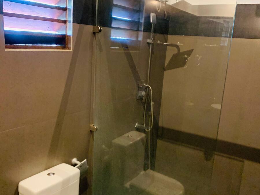 Et badeværelse med en glasafskærmet bruseniche, toilet og et vindue med skodder.