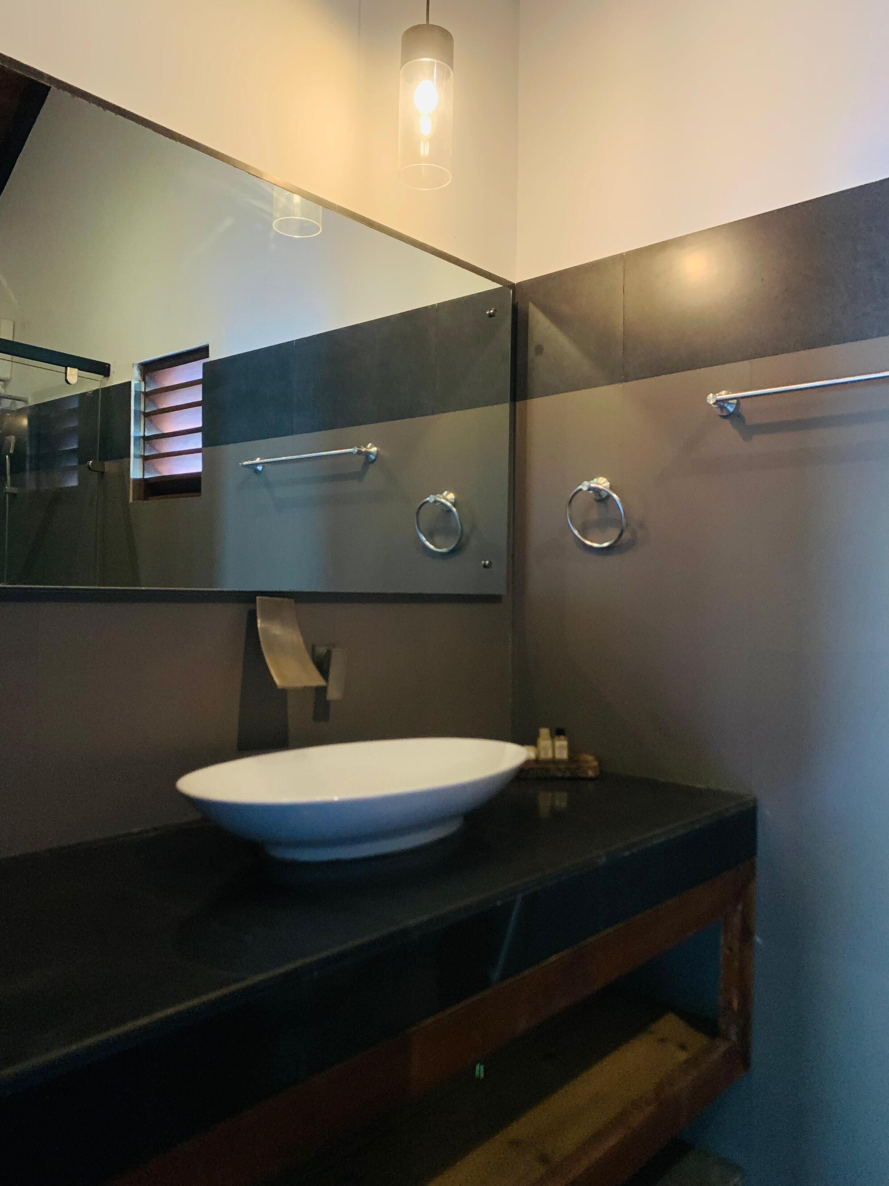 Une salle de bain moderne avec un grand miroir, un lavabo blanc et un porte-serviettes.